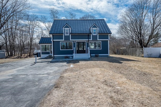 view of front of property with a standing seam roof, fence, driveway, and metal roof