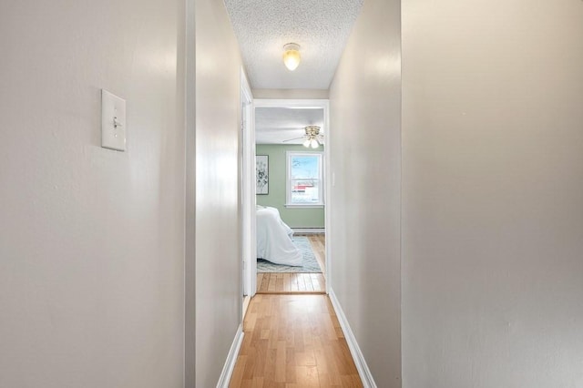 corridor featuring baseboards, a textured ceiling, and light wood finished floors