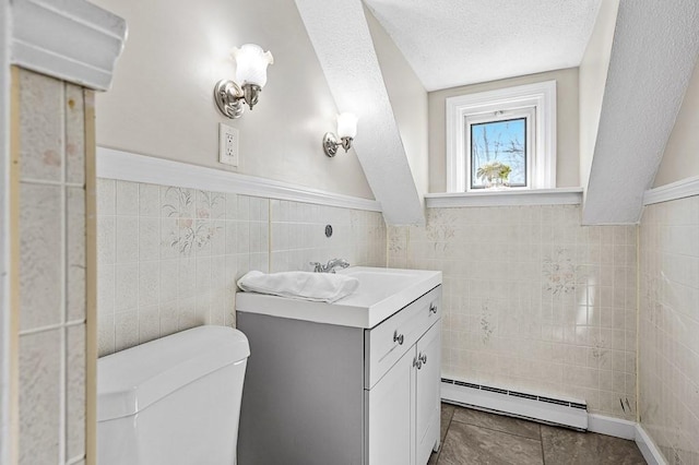 half bath featuring a baseboard heating unit, toilet, vanity, a textured ceiling, and tile walls