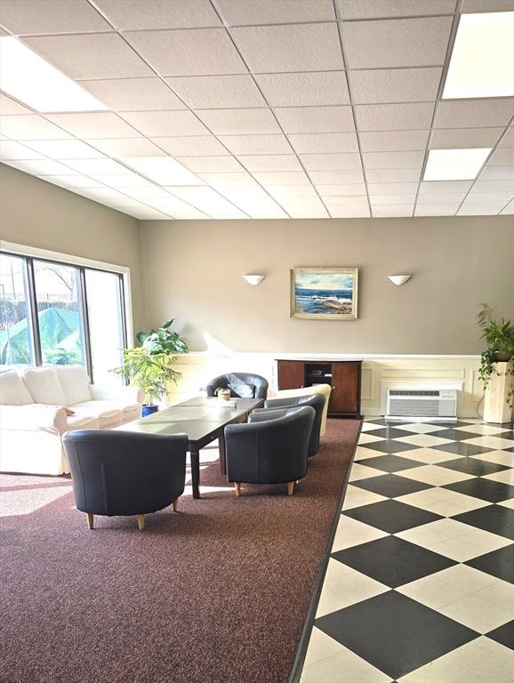 living room with an AC wall unit and a paneled ceiling