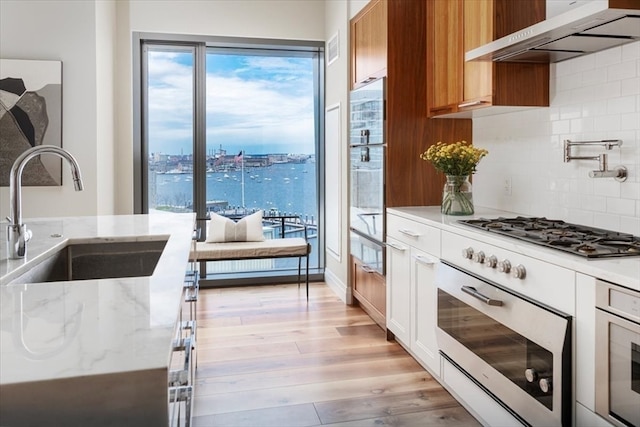 kitchen with a water view, white cabinets, exhaust hood, light wood-type flooring, and sink