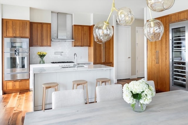 kitchen featuring sink, a kitchen bar, wall chimney exhaust hood, backsplash, and hardwood / wood-style floors