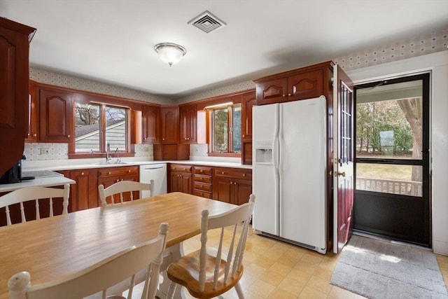 kitchen featuring light countertops, visible vents, white appliances, light floors, and a sink