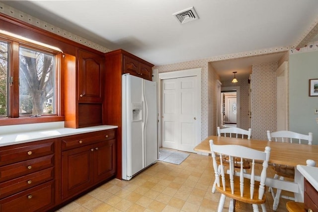 kitchen featuring white refrigerator with ice dispenser, wallpapered walls, light countertops, and visible vents