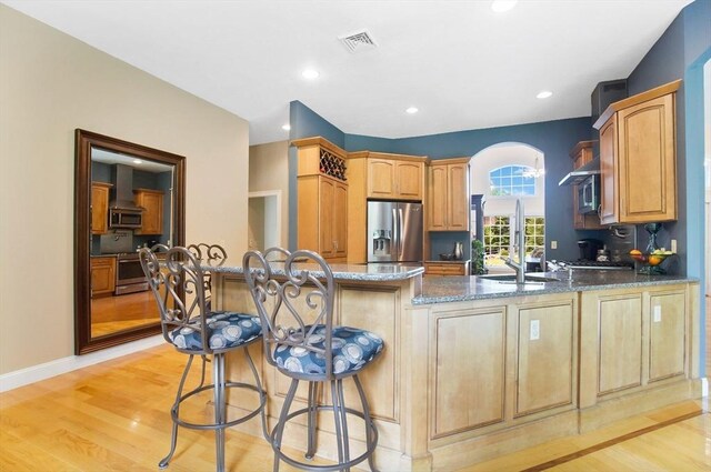 kitchen featuring appliances with stainless steel finishes, kitchen peninsula, dark stone countertops, light hardwood / wood-style floors, and a breakfast bar