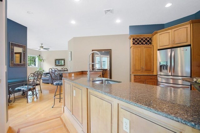 kitchen with dark stone countertops, stainless steel fridge with ice dispenser, ceiling fan, sink, and light hardwood / wood-style floors