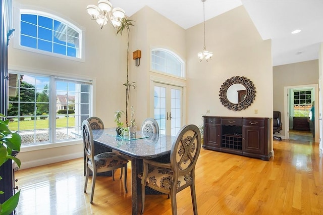 dining space featuring french doors, a high ceiling, an inviting chandelier, and light hardwood / wood-style floors