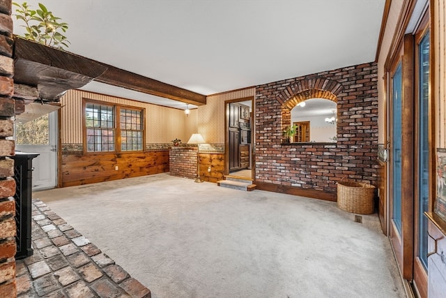 unfurnished living room with brick wall, beamed ceiling, carpet flooring, and wooden walls