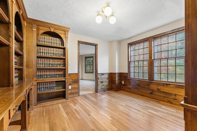 interior space featuring wood walls, a textured ceiling, and light hardwood / wood-style flooring