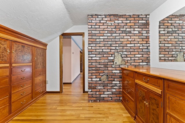 corridor with vaulted ceiling, light hardwood / wood-style flooring, and a textured ceiling