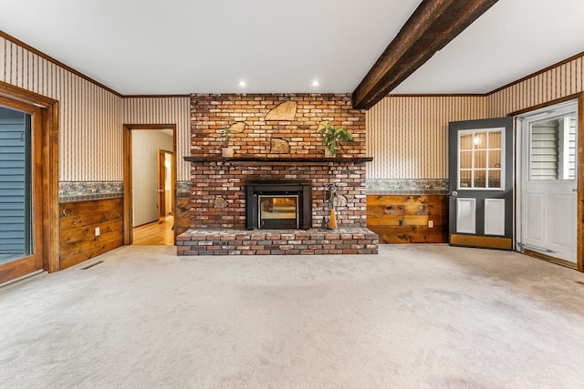 unfurnished living room with wood walls, beam ceiling, light colored carpet, and a fireplace