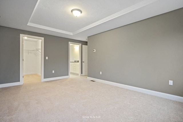 unfurnished bedroom featuring crown molding, a walk in closet, a closet, and light colored carpet