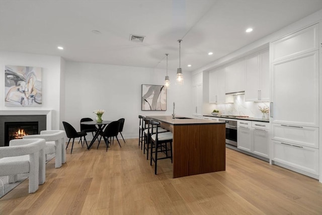 100 Linden St Unit 102, Wellesley, MA 02482 - kitchen featuring appliances with stainless steel finishes, a sink, a kitchen bar, light wood finished floors, and a center island with sink