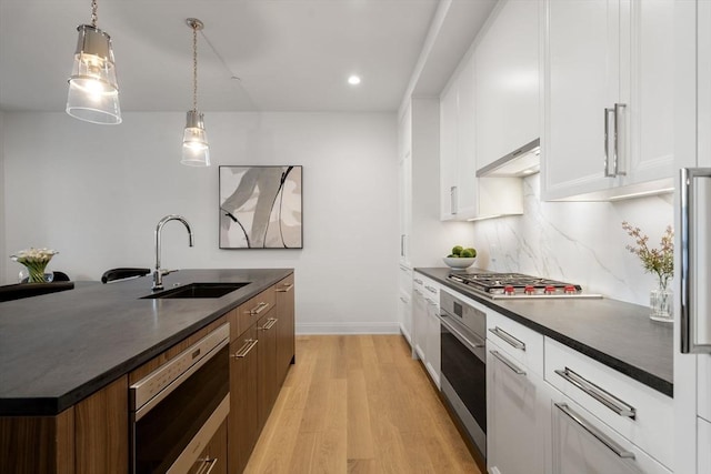100 Linden St Unit 102, Wellesley, MA 02482 - kitchen featuring a sink, dark countertops, stainless steel appliances, light wood-type flooring, and white cabinetry
