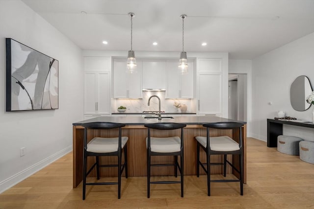 100 Linden St Unit 102, Wellesley, MA 02482 - kitchen featuring white cabinetry, backsplash, an island with sink, dark countertops, and light wood finished floors