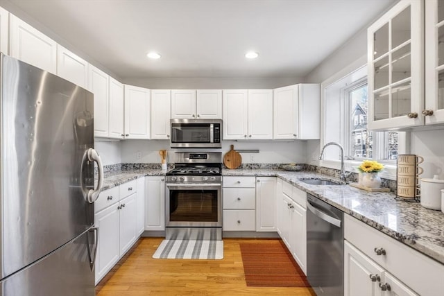 kitchen featuring sink, white cabinetry, light stone counters, light wood-type flooring, and appliances with stainless steel finishes