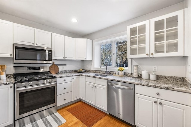 kitchen with sink, appliances with stainless steel finishes, white cabinetry, light stone counters, and light wood-type flooring