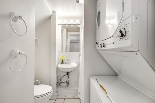 bathroom featuring tile patterned floors, stacked washer and clothes dryer, and toilet