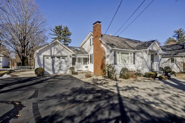 view of front of house with aphalt driveway, an attached garage, fence, and a chimney