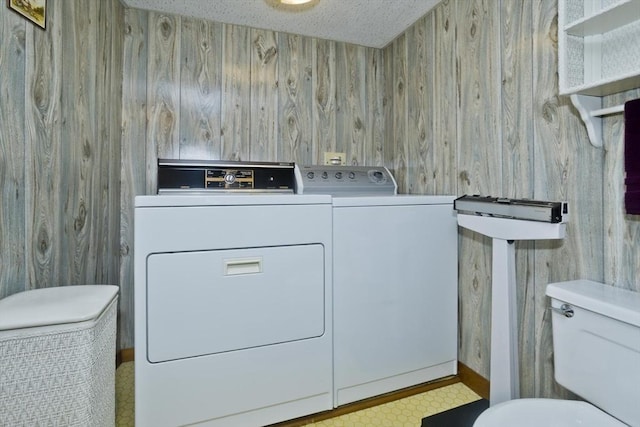 clothes washing area with a textured ceiling, laundry area, wood walls, and washing machine and clothes dryer