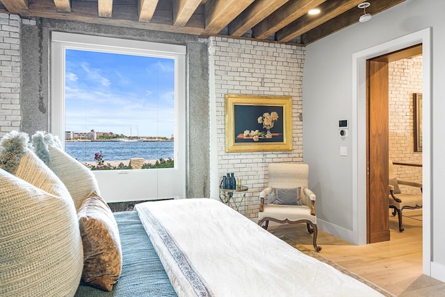 bedroom featuring a water view, brick wall, wood-type flooring, and beam ceiling