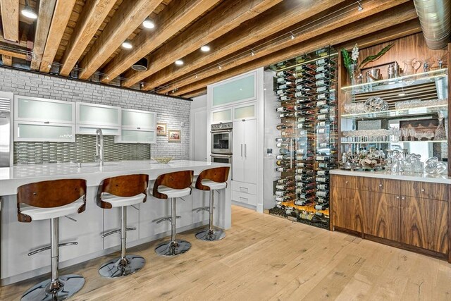 wine cellar featuring beamed ceiling, wet bar, and light hardwood / wood-style floors