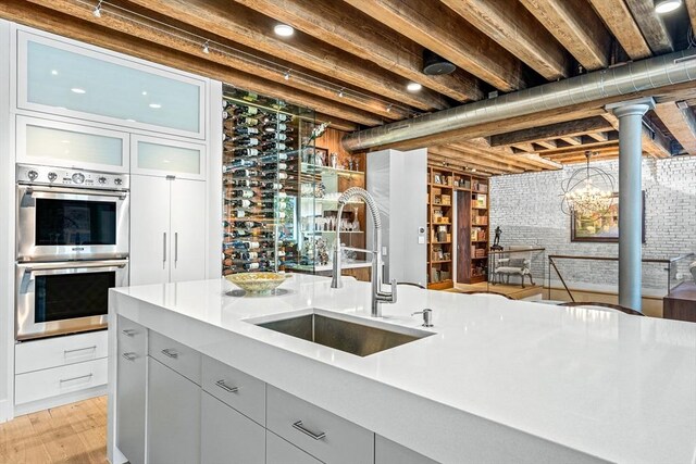 kitchen featuring brick wall, light hardwood / wood-style flooring, sink, and double oven