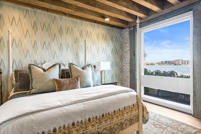 bedroom featuring a water view, wood-type flooring, multiple windows, and beam ceiling