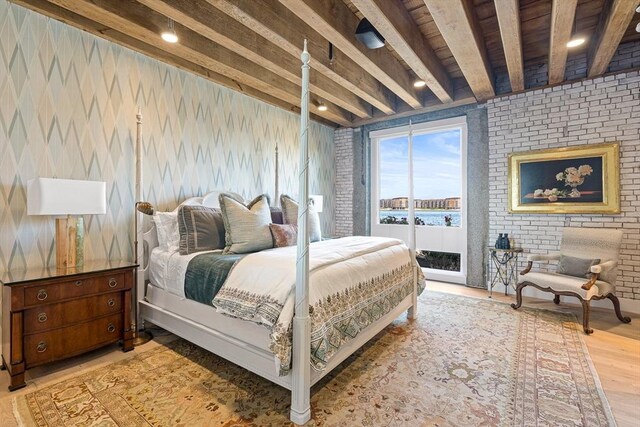 bedroom featuring beamed ceiling, brick wall, access to exterior, and light hardwood / wood-style floors