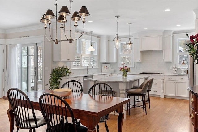 dining room featuring light wood-type flooring, plenty of natural light, ornamental molding, and a chandelier