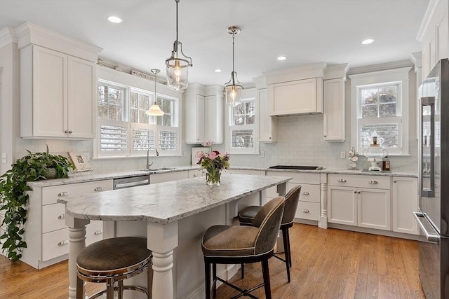 kitchen with decorative light fixtures, white cabinets, a kitchen island, a sink, and a kitchen bar