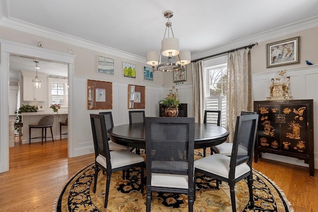 dining room with ornamental molding, wainscoting, light wood-style flooring, and a decorative wall