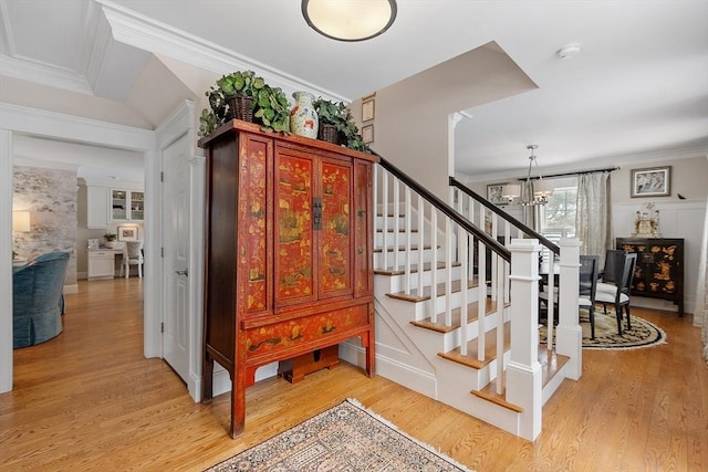 stairway featuring an inviting chandelier, ornamental molding, and wood finished floors