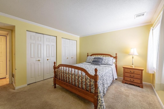 bedroom featuring a textured ceiling, crown molding, light colored carpet, and two closets