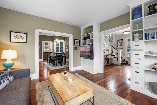 living area with stairs, dark wood-style flooring, baseboards, and a chandelier