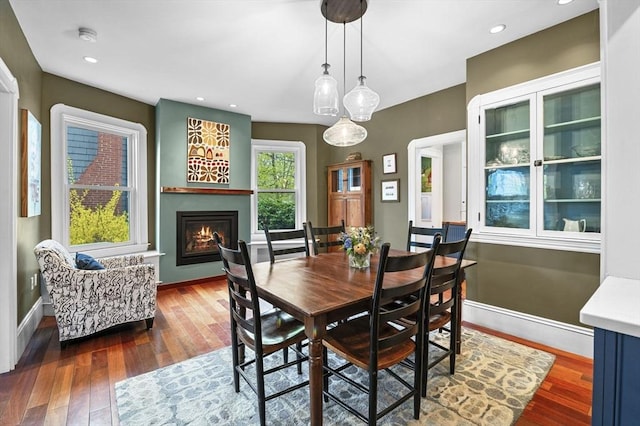 dining room featuring baseboards, hardwood / wood-style floors, a glass covered fireplace, and recessed lighting