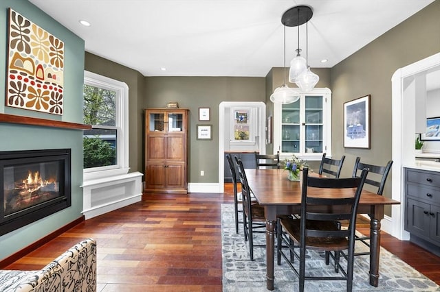 dining room featuring baseboards, dark wood-style floors, a glass covered fireplace, and recessed lighting