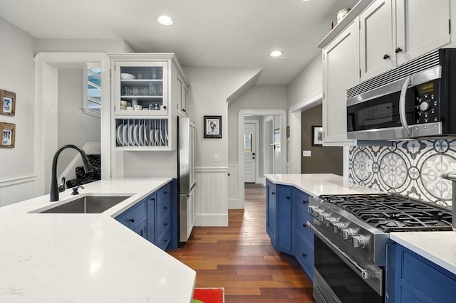 kitchen with high end appliances, dark wood-style floors, a sink, and blue cabinetry