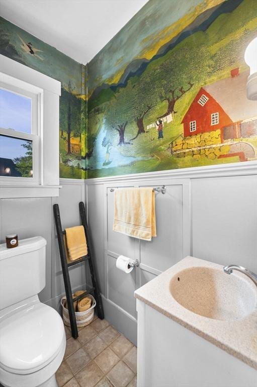 half bath featuring toilet, a decorative wall, wainscoting, and a sink
