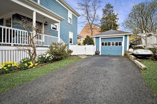 view of side of home featuring covered porch, fence, aphalt driveway, an outbuilding, and a detached garage