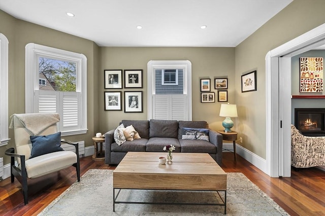 living room featuring recessed lighting, baseboards, a glass covered fireplace, and dark wood finished floors