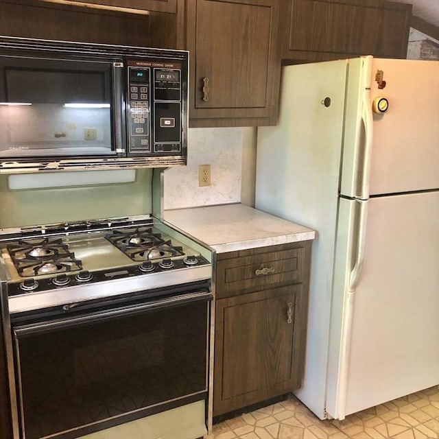 kitchen featuring freestanding refrigerator, black microwave, gas range oven, light countertops, and dark brown cabinets