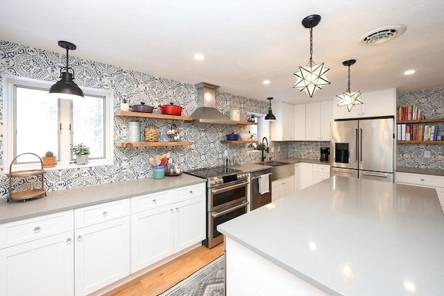 kitchen featuring stainless steel appliances, white cabinetry, decorative light fixtures, and wall chimney exhaust hood