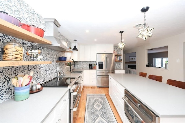 kitchen with decorative light fixtures, sink, white cabinets, stainless steel appliances, and wall chimney range hood