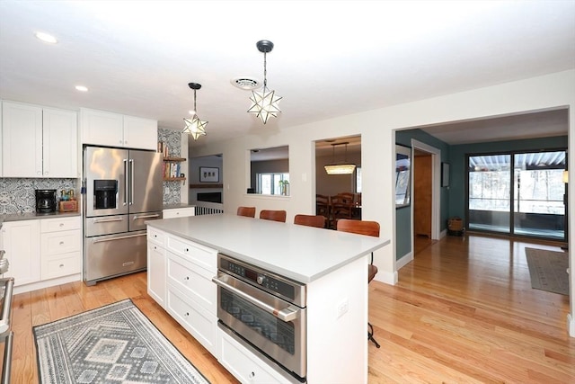 kitchen with a kitchen island, appliances with stainless steel finishes, white cabinets, a kitchen breakfast bar, and hanging light fixtures