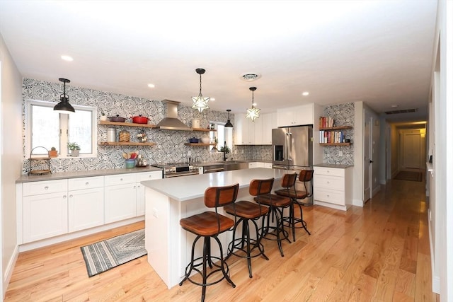 kitchen featuring wall chimney exhaust hood, a kitchen bar, appliances with stainless steel finishes, a kitchen island, and white cabinets