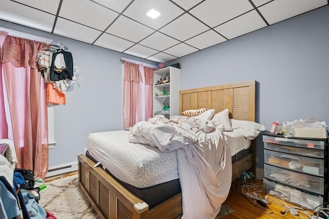 bedroom featuring light hardwood / wood-style floors, baseboard heating, and a paneled ceiling