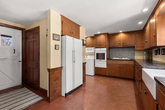 kitchen with washer / dryer, white appliances, brown cabinets, and a warming drawer