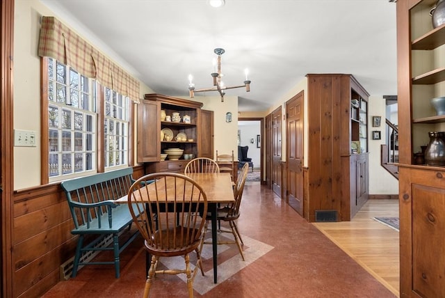 dining room with wooden walls, wood finished floors, visible vents, and a notable chandelier