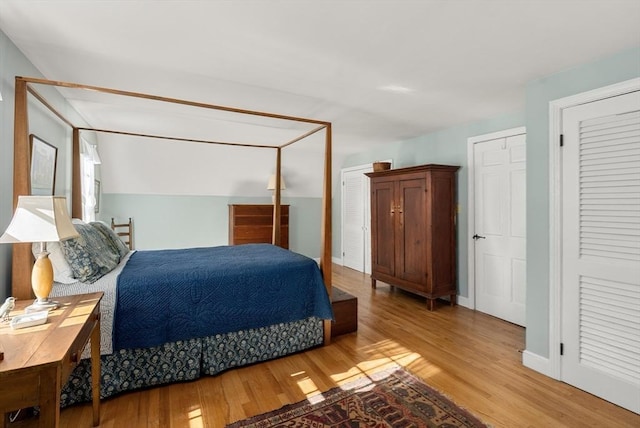 bedroom featuring light wood-style floors, lofted ceiling, baseboards, and two closets